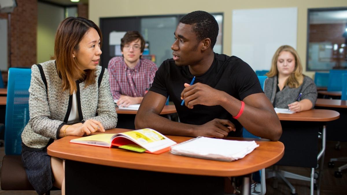 Professor and student in classroom discussion with  other students in the background 