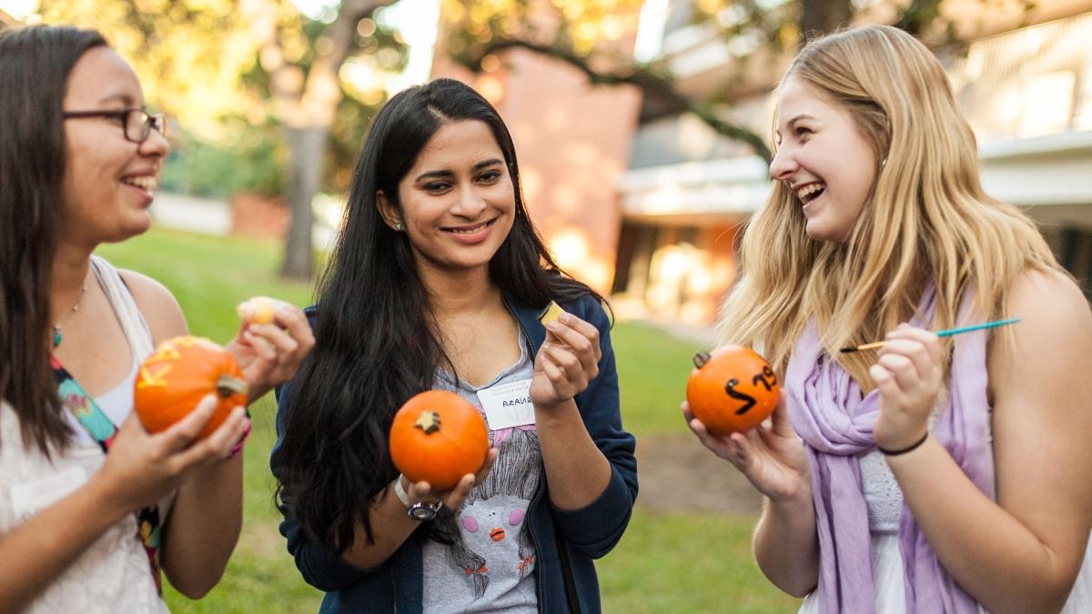 Three women are painting details on small pumpkins in the first-year quad